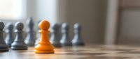 Young orange pawn standing out among gray pawns on chessboard, symbolizing leadership, uniqueness, and strategic advantage in business and competition.