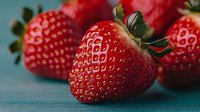 Fresh ripe strawberries with green leaves on turquoise wooden background, macro shot showing detailed texture and natural pattern of berries.