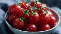 Fresh ripe cherry tomatoes with water drops on vine in gray ceramic bowl, close up view with selective focus and natural lighting.