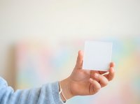 Person holding blank white card with one hand against soft pastel gradient background, suitable for business cards, promotional materials, and marketing designs.