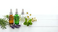 Essential oils in glass dropper bottles with fresh herbs including rosemary, lavender, mint and chamomile flowers on white wooden background for aromatherapy.