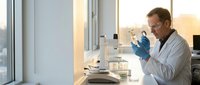 Male scientist in white lab coat examining test tube sample in modern laboratory with microscope and equipment during research work.