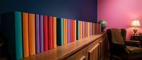 Colorful book spines arranged on wooden shelf in modern library room with pink neon lighting and leather armchair for interior design and home decor projects.