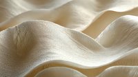 Soft waves of cream-colored fabric create gentle folds and shadows, showcasing luxurious textile texture with delicate light play for fashion and interior design backgrounds.