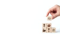 Hand placing wooden cube with flower icon completing nature symbol collection on white background for eco-friendly business concepts.