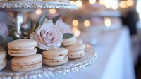 Delicate pink rose and vanilla macarons on crystal serving platter with soft bokeh lights creating romantic wedding reception or party atmosphere.