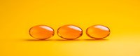 Transparent orange gel capsules arranged in row on vibrant yellow background. Medical supplement pills with soft shadow and reflection for pharmaceutical design.