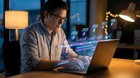 Professional businessman working late at office desk with laptop computer analyzing financial data and yearly statistics in modern workspace with warm lighting.