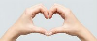 Two hands forming a heart shape gesture on a light gray background, symbolizing love, care, and connection.
