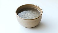 Ceramic bowl filled with white crystalline salt on light background, traditional pottery container with natural mineral seasoning for cooking and food preservation.