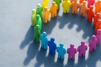 Colorful paper cut figures standing in circle casting shadow on gray surface, representing diversity, unity and teamwork in business community.