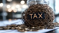 Nest shaped from tangled wires with word TAX, surrounded by scattered coins on dark surface against blurred bokeh background, representing financial burden.