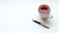 White ceramic cup filled with black tea next to elegant fountain pen on clean white background for business and writing concepts.