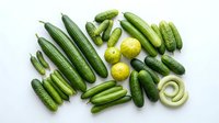 Fresh green vegetables collection with cucumbers, zucchini, peas, lime and onion arranged on white background for healthy cooking and nutrition concepts.