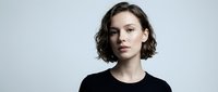Young Caucasian woman with short brown wavy hair wearing black shirt against white background, professional headshot portrait for business branding.