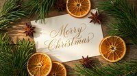Merry Christmas greeting card on rustic wooden table with dried orange slices, star anise, and pine branches in warm holiday flat lay.