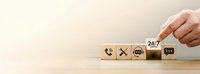 Hand placing wooden blocks with customer service icons including phone, email and 24/7 support symbols on desk for business communication concept.