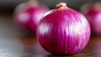 Fresh red onion with vibrant purple skin on dark wooden surface, selective focus on foreground bulb with soft blurred background creates depth.