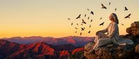 Young woman sitting on mountain cliff watching birds fly at golden sunset with layered mountain ranges creating peaceful meditation scene for wellness content.