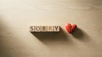 Wooden letter cubes spelling SORRY next to a broken red heart on a light wood surface, symbolizing apology, regret, and relationship pain.