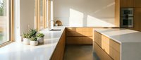 Modern kitchen with wooden cabinetry, white countertops, and natural light from large windows. Minimalist design with potted plant and open shelving for contemporary home interiors.