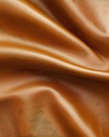 Smooth flowing caramel brown satin fabric with elegant folds and waves creating luxurious texture and light reflections. Seamless pattern suitable for backgrounds.