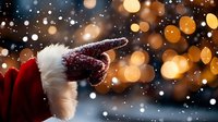Santa Claus hand in red glove with white fur trim pointing up against blurred golden bokeh lights and falling snow creating magical holiday atmosphere.