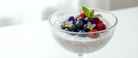 Chia seed pudding topped with fresh blueberries and raspberries in glass bowl on white surface for healthy breakfast or dessert recipes.