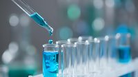 Laboratory pipette dropping blue chemical solution into test tube for scientific research and medical analysis in modern lab setting.