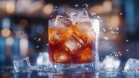 Glass of cold cola drink with ice cubes and splashing droplets on dark background with bokeh lights, refreshing carbonated beverage for restaurant menu.
