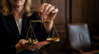 Professional female lawyer holding golden scales of justice in courtroom setting, representing legal expertise and judicial fairness in law practice.