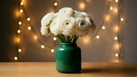 White ranunculus flowers in emerald green vase on wooden table with warm bokeh lights background for home decor and floral arrangements.