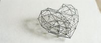 Geometric heart wireframe sculpture made of black metal lines creating polygonal love symbol on white surface for modern decor and romantic design projects.