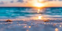 Golden sunset over turquoise ocean waves with sparkling sand in foreground, creating dreamy bokeh effect and peaceful beach atmosphere at dusk.