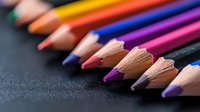 Vibrant colored pencils arranged in diagonal line on dark background, sharp tips in focus showing wood texture and lead detail. For art and education concepts.
