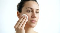 Young woman applying skincare product with cotton pad on face during daily beauty routine for healthy glowing skin and facial care regimen.