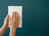 Person with light skin tone holding open book with blank pages against teal background, suitable for education, reading, and learning concepts.