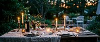 Elegant outdoor dinner table setting with candles and wine glasses in garden at twilight for romantic dining and entertaining occasions.