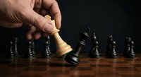 Hand moving white king chess piece in strategic game with black pieces on wooden board against dark background for business planning concepts.
