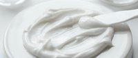 Creamy white cosmetic or dairy product with wooden spatula on white plate, suitable for skincare, beauty, or food packaging design.