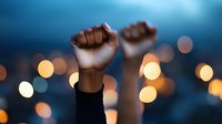 Raised fists silhouetted against blurred city lights at dusk, symbolizing protest, unity, and social movement activism in urban setting. Powerful emotional scene.