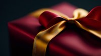 Elegant burgundy gift box with luxurious golden satin ribbon bow against dark background, shallow depth of field creates soft dreamy holiday atmosphere.
