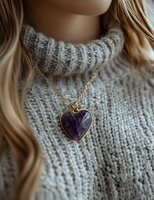 Close-up of amethyst heart pendant necklace on gold chain against gray knit sweater background, with soft blonde hair framing the composition.