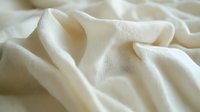 Soft ivory fabric with gentle folds and creases creates luxurious texture and depth. Natural light enhances subtle shadows on cream textile surface.