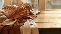 Dried palm leaf on rustic wooden table with linen fabric near window, warm earthy tones creating cozy boho interior decor atmosphere.