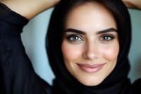 Young woman with dark hair and olive complexion wearing black hijab, smiling at camera with natural makeup and confident expression for portrait and lifestyle use.