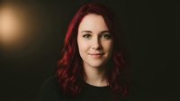 Young Caucasian woman with red hair smiling confidently in professional portrait with warm lighting against dark background for business headshots.
