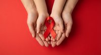 Hands holding red awareness ribbon on red background symbolizing support for health causes and solidarity in medical advocacy campaigns.