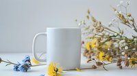White ceramic mug mockup with spring wildflowers and branches on neutral background for branding and design projects.