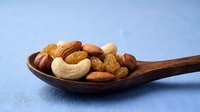 Mixed nuts including almonds cashews and walnuts in wooden spoon on blue background for healthy snacking and cooking recipes.